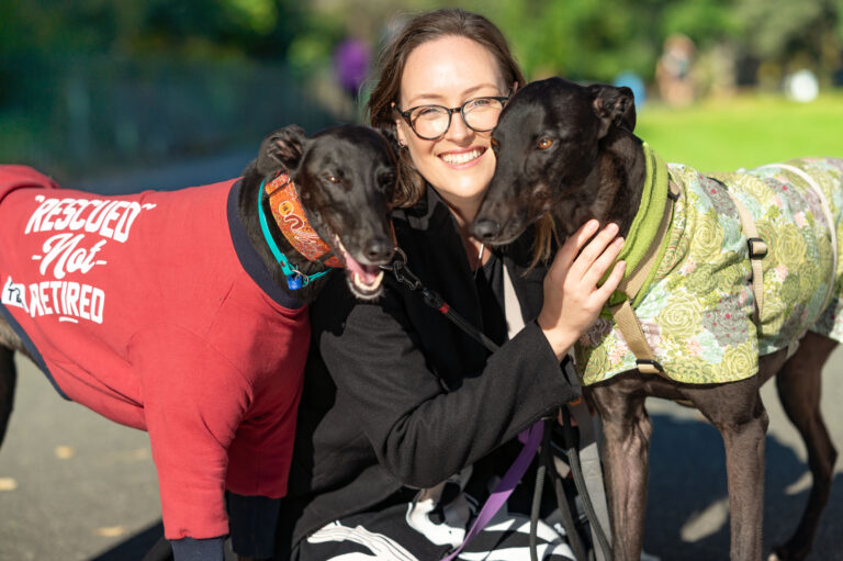 Katherine Copsey MP with two black greyhounds. One is wearing a green coat and the other is wearing a red coat that reads "Rescued, not retired"