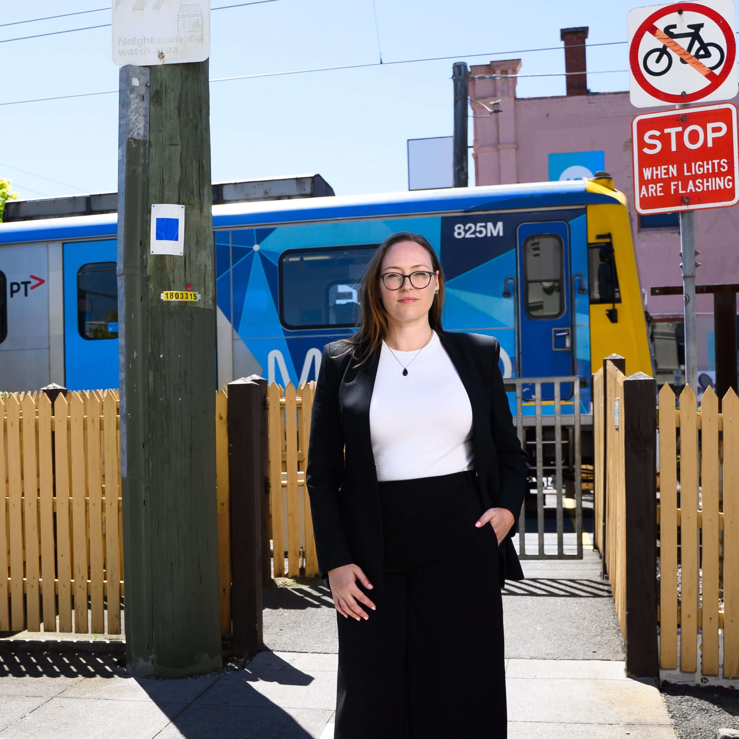 Katheine Copsey MP standing in front of a level pedestrian crossing as a Metro train passes behind her