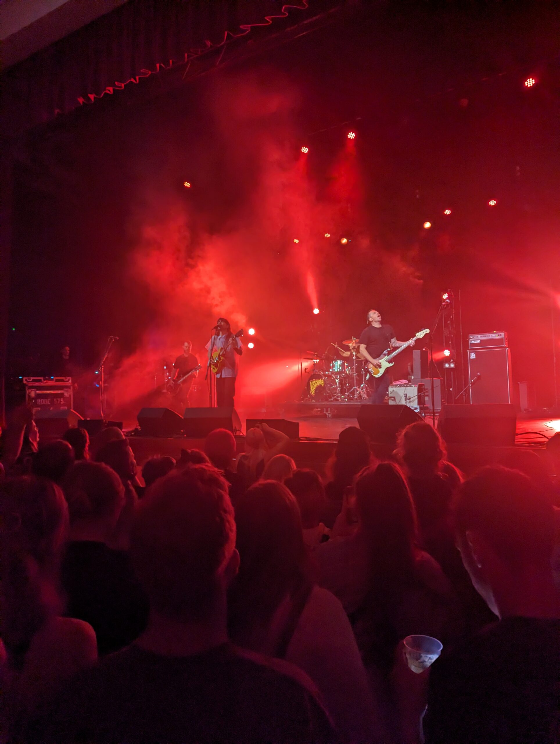 A band playing a gig in front of a crowd, bathed in red stage lights